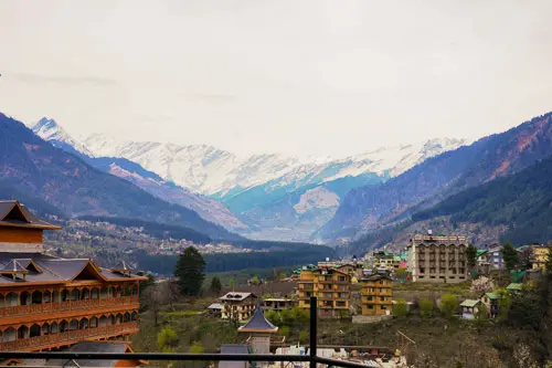 Panoramic view of Manali valley with snow-covered Himalayan mountains and traditional wooden architecture